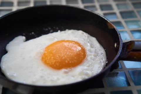 Two 2 Fried salt eggs in skillet pan on blue checkered background close up, top Stock Photos