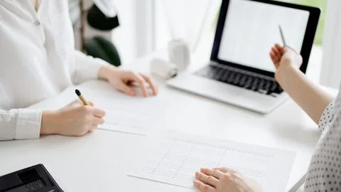 Two accountants using a laptop computer for counting taxes at white desk in Stock-Fotos