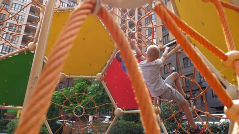 Two active boys climb a rope slide on the playground in the courtyard. Stock Footage 331696783