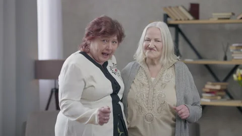 Two active senior women dancing in living room looking at camera. Portrait of Stock Footage 156039501