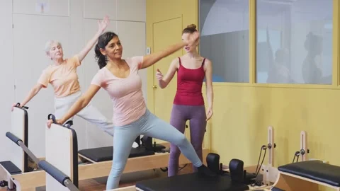 Two active women of different ages, practicing Pilates in a fitness studio to Stock Footage 323906356