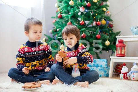 Two adorable children, boy brothers, eating cookies and drinking milk at home Stock Photos