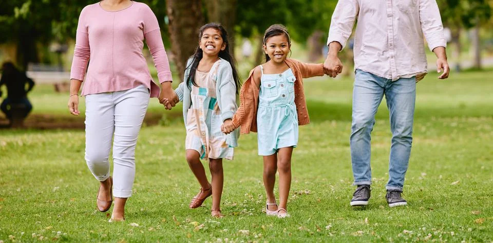 Two adorable little girls walking outside in park with parents. Sibling sisters Stock Photos