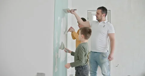 Two adults and a child, each involved in applying paint, DIY home improvement Stock Footage 273494681