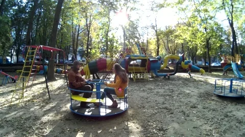 Two adults have fun on the carousel in a park outside view Stock Footage 68674286