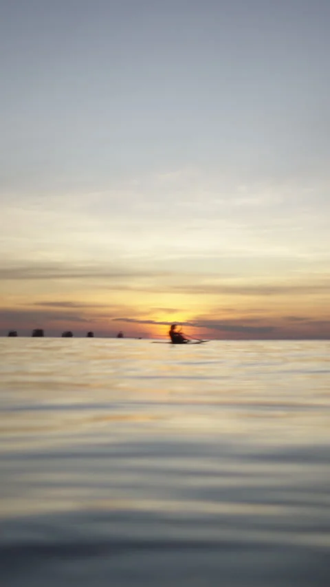 Two adults paddling in the background at sunset in the sea Stock Footage 265470367