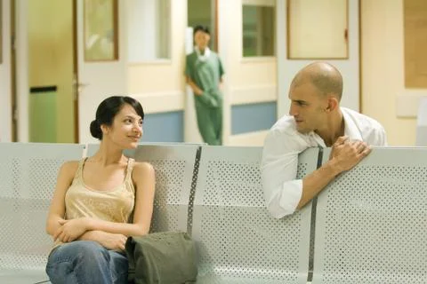 Two adults sitting in hospital waiting room, chatting Stock Photos