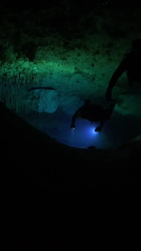 Two adventurous divers swimming and exploring a dark, submerged cave with Stock Footage 332002662