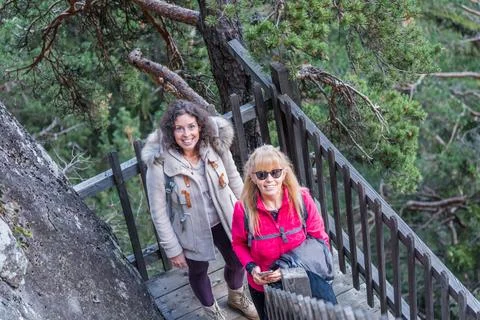 Two adventurous women smiling while walking on a hiking trail in nature. Stock Photos