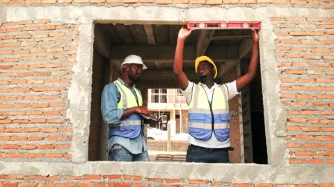 Two African construction workers in safety gear use a spirit level on a brick Video stock 321448822