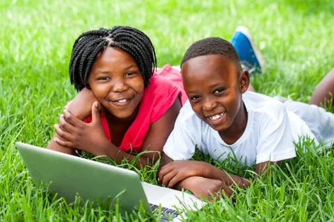Two african kids laying on grass with laptop. Stock Photos