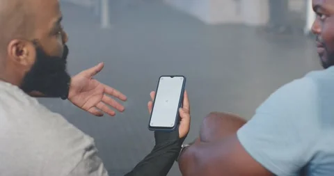 Two African men in gym left holding phone showing loading spinner explaining Stock Footage 338326206
