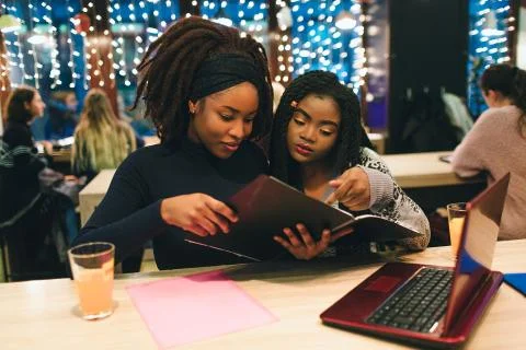 Two african students look at opened journal. They sit and study. They have red Stockfoto's