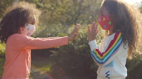 Two afro girls in safety mask playing hand clapping game outdoors Stock Footage