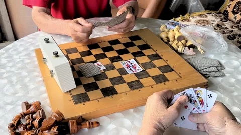 Two aged men playing cards on a chess board on white table in the garden at Stock Footage 243636681