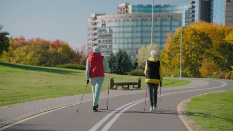 Two aged women doing Nordic walking in fall city park on a sunny day, back view 스톡 동영상 165306331