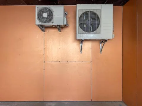 Two air conditioners or heat pumps are mounted on wall behind building Stock Photos