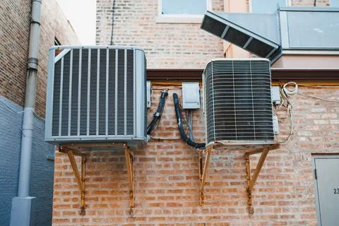 Two air conditioning units are installed on a brick wall in an urban area. Th 스톡 사진