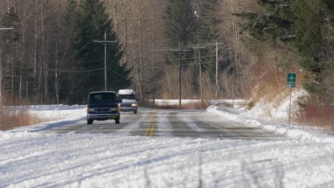 Two Airport Shuttle Vans Round Corner in Snowy Winter Sunshiny Day Low Angle Stock Footage 107130715