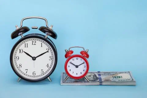Two alarm clock stands on a stack of money on a blue background Stock Photos