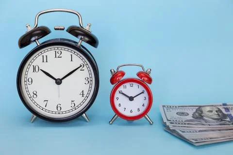Two alarm clocks stands on a stack of money on a blue background Stock Photos