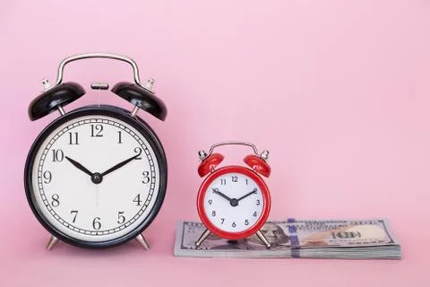 Two alarm clocks stands on a stack of money on a pink background Stock Photos