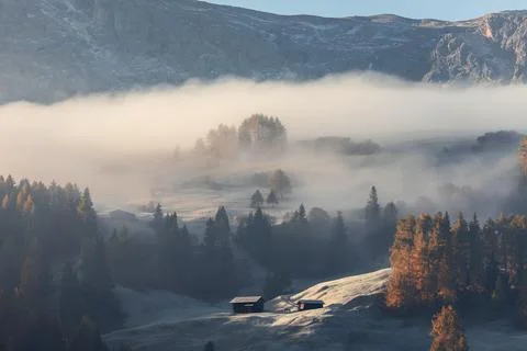 Two alpine huts on a hill of Seiser Alm plateau covered with morning mist and Stock Photos