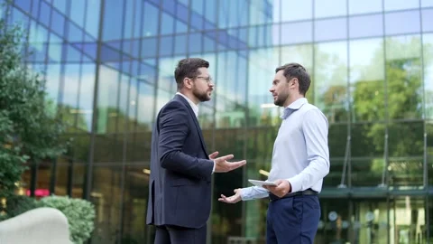 Two angry businessmen standing outdoors outside near an office building argue  Stock Footage 332472441