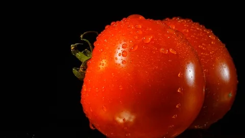 Two appetizing ripe tomatoes on a mirror black background. Rotating table and Stock Footage 94804341