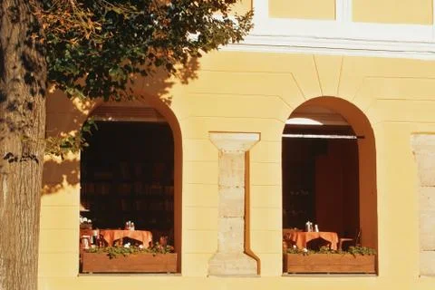 Two arch-formed windows of cafe, two tables with red tablecloth, a yellow old Stock-Fotos