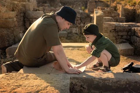 Two archeologists, child and adult, in khaki clothes sitting on ruins and Stock Photos