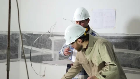 Two architects analyze a drawing of a building while standing indoors Stock Footage 235541329