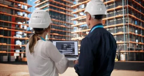Two Architects And Engineer Discuss 3D BIM Model On Busy Construction Site. Stock Photos