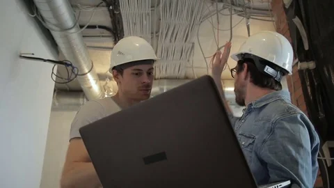 Two architects in helmets talking looking at laptop standing at construction Video stock 78120253