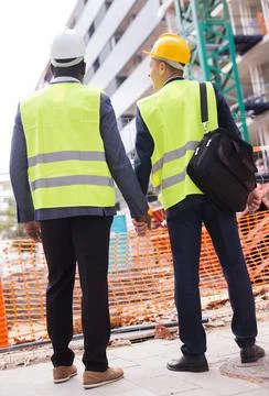 Two architects in protective helmets and jacket look at the unfinished house Stock Photos