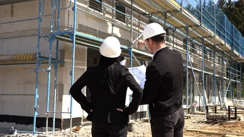 Two architects in white helmets discuss a plan at a construction site 動画素材 107411028