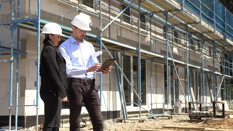 Two architects in white helmets discuss a plan at a construction site Vídeos de archivo 107526706