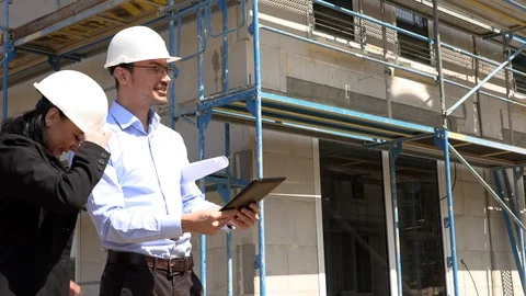 Two architects in white helmets discuss a plan at a construction site Видео 107526813