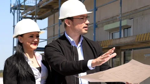 Two architects in white helmets discuss a plan at a construction site Stock Footage 107527396