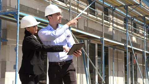 Two architects in white helmets discuss a plan at a construction site 動画素材 107527664