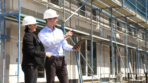 Two architects in white helmets discuss a plan at a construction site 動画素材 107528445