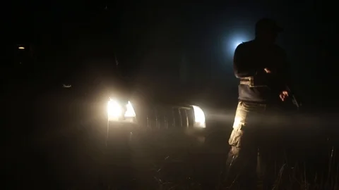 Two armed men stand on the street at night. headlights partially illuminate them Stock Footage 124785511