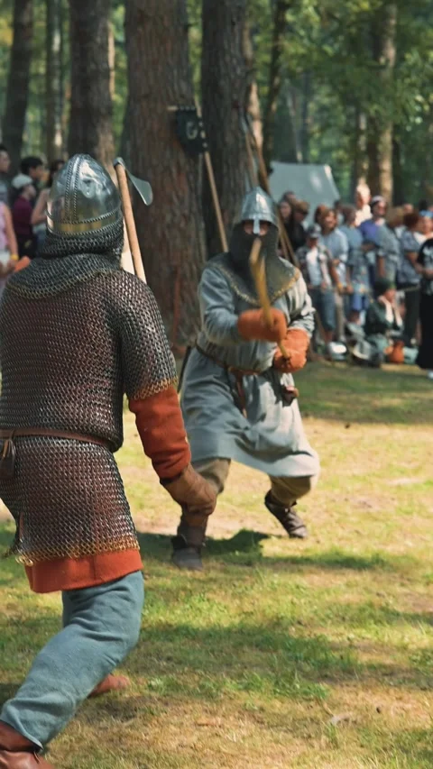 Two armored fighters engage in a mock battle in a wooded area filled with Видео 345030153