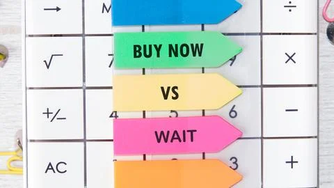 Two arrows point to buy now and wait choices placed on a calculator while mak Stock Photos