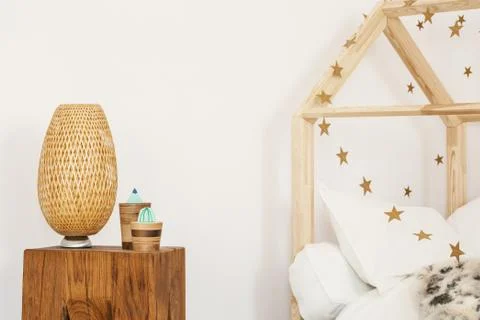 Two artificial cactuses and wicker lamp standing on wooden bedside table in w Stock Photos
