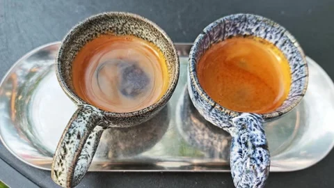 Two artisan ceramic cups of hot espresso with golden crema on a tray. 스톡 동영상 339780526