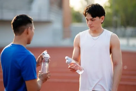 Two asian athlete men are looking at their water bottles while talking toge.. Stock Photos