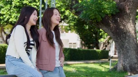 Two Asian Female Students Talking and Laughing on University Campus Park Bench Stock Footage 339994063