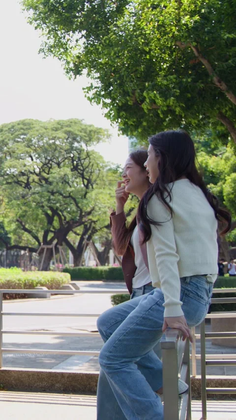 Two Asian Female Students Talking and Laughing on University Campus Railing Stock Footage 342583611