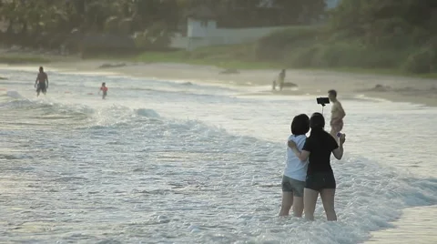 Two asian girls are taking selfie amid the beautiful surf, using smartphone. Stock Footage 44683300